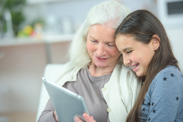 Granddaughter and grandmother laughing while looking at tablet - Photo, Image