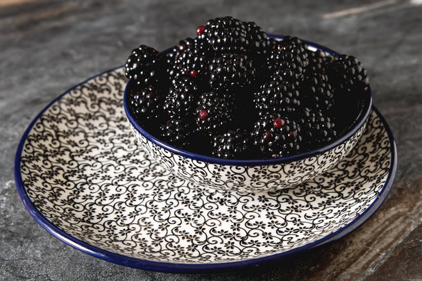 Blackberry in a ceramic plate. Dark background. Sweet berry. - Фото, изображение