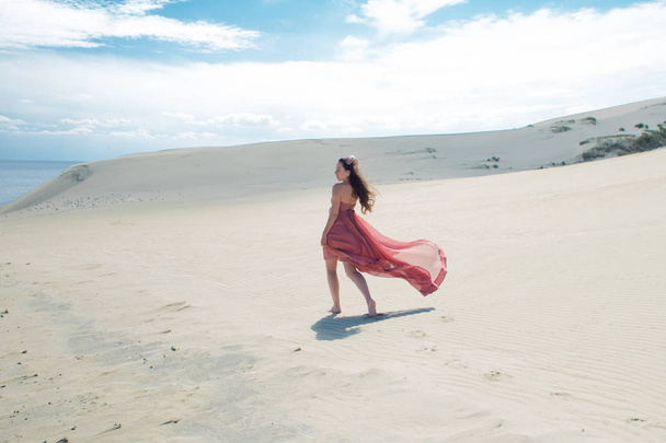 Woman in red waving dress with flying fabric runs on background of dunes. Enjoy the freedom - Fotó, kép