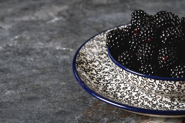 Blackberry in a ceramic plate. Dark background. Sweet berry. - Photo, image