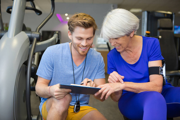 personal trainer assist senior woman exercising on machine at gym - Valokuva, kuva