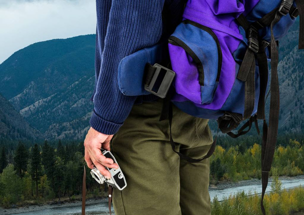 Millennial backpacker mid section holding camera against river and hills - Foto, Imagem