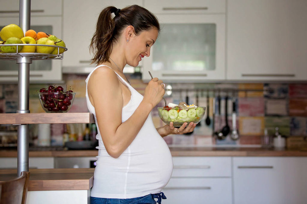 Happy pregnant woman eating salad at home - 写真・画像