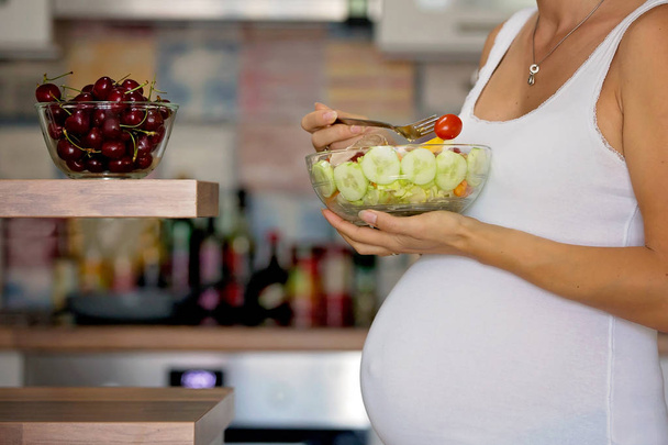 Happy pregnant woman eating salad at home - Fotó, kép