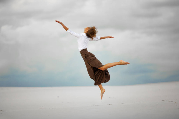 Young woman jumps on sand in desert and joyful laughs. - Photo, Image