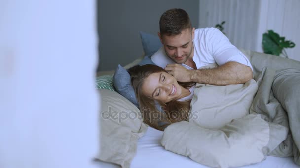 Young beautiful and loving couple wake up at the morning. Attractive man kiss and hug his wife in bed - Footage, Video