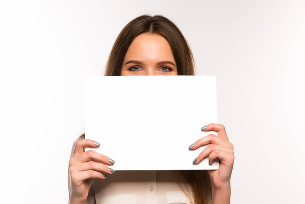 The girl is holding a sheet of blank paper in front of her - Φωτογραφία, εικόνα
