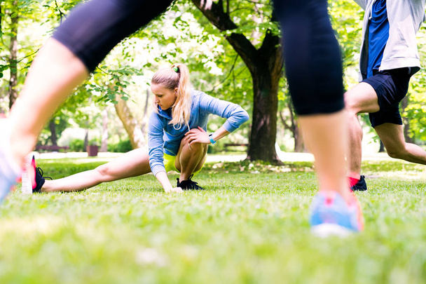 Group of young runners stretching and warming up in park. - 写真・画像