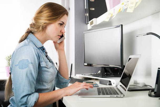 Woman working at home office while talking on phone - Photo, image