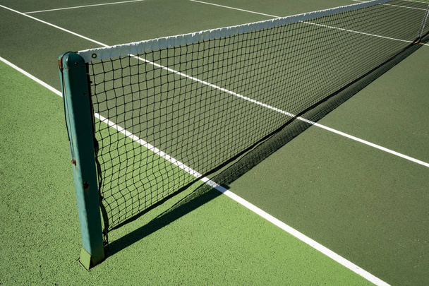 Red de tenis ensartada a través de pista de tenis artificial resistente
 - Foto, imagen