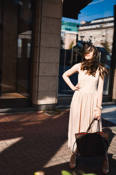 portrait of a slender young girl blogger beautiful brunette in downtown dusseldorf in a pastel dress and a lady wearing sunglasses walking poses and smiling on the sunset - Фото, зображення