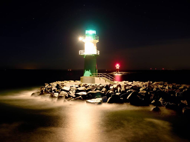 Grüner Leuchtturm leuchtet am Ende der steinigen Seebrücke in dunkler Nacht - Foto, Bild
