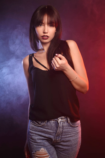 Beautiful brunette girl in a shirt and jeans steps into the smoke - Photo, Image