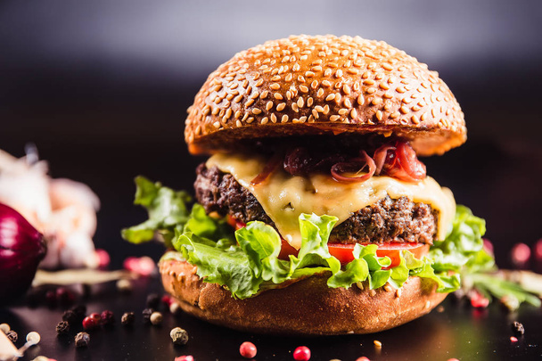Juicy delicious burger with spices on a black background - Фото, изображение