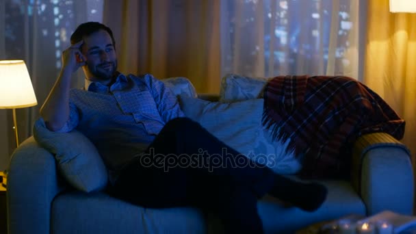 Ve středu večer člověk doma sám sedí na gauči a sledování televize. Dívá se bavit. Jeho okna mají výhled na velké město s mrakodrapy. - Záběry, video
