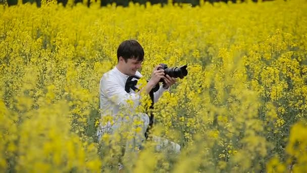Valokuvaaja kameran kanssa ottamassa kuvia kukkivalla keltaisella kentällä
 - Materiaali, video