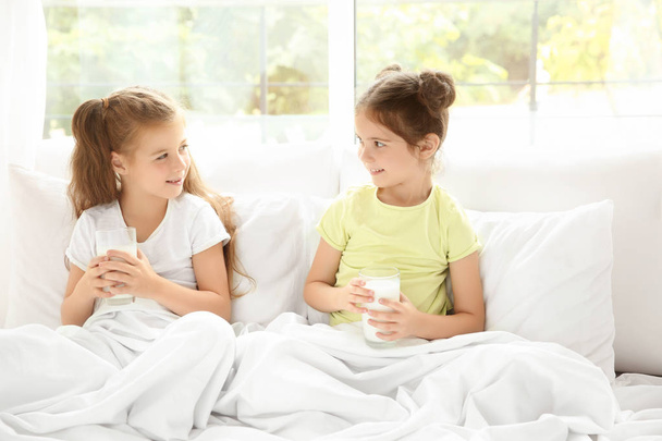 Portrait of two little girls in bed with glasses of milk - 写真・画像
