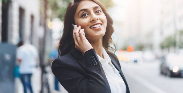 Close-up πορτρέτο του ελκυστικού επιχειρηματικού γυναίκα φοράει μοντέρνο κοστούμι και μιλώντας στο smartphone, ενώ πρόκειται να εργάζονται στο αστικό δρόμο - Φωτογραφία, εικόνα