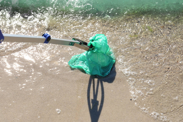 Young person cleaning beach area with trash picker. Volunteer concept - Foto, Imagem