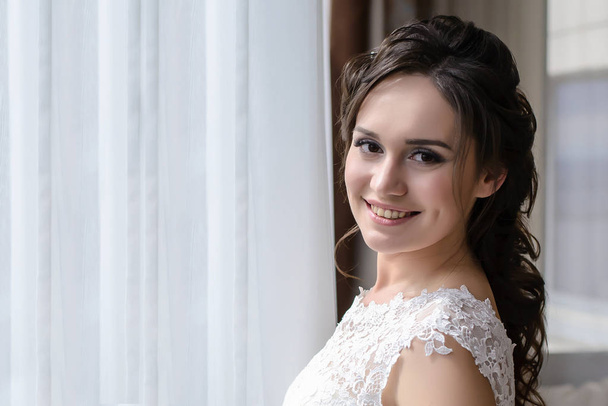 Beautiful bride stands at the window and smiles in the morning - Photo, image