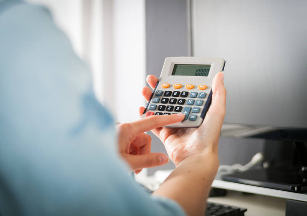 Woman at home office using calculator, calculating budget - Photo, image
