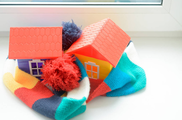 Toy house on the window sill wrapped in a scarf. Warming up the house. - Photo, Image