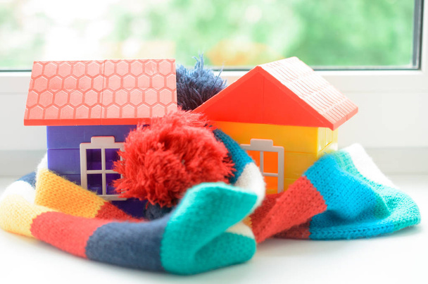Casa de juguetes en el alféizar de la ventana envuelta en una bufanda. Calentando la casa
. - Foto, imagen