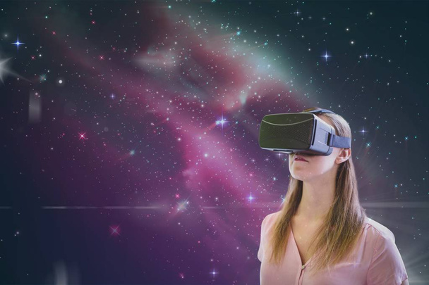 Woman in VR headset looking against pink galaxy background - Foto, afbeelding
