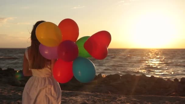 Dziewczyna z kolorowych balonów na plaży o zachodzie słońca - Materiał filmowy, wideo