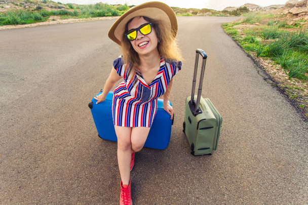 Onnellinen matkustaja nainen istuu matkalaukku tiellä ja hymyilee. Käsite matka, matka, matka
 - Valokuva, kuva