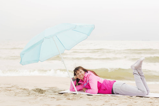 Photo of beautiful girl in a coat lying on a sandy beach - Photo, Image