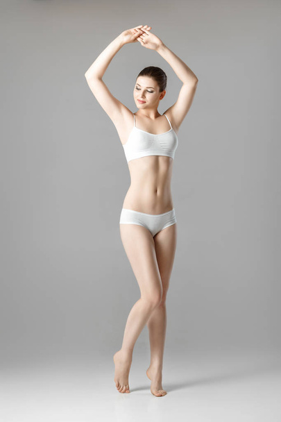 slim beautiful woman with perfect body in white lingerie on gray background - 写真・画像
