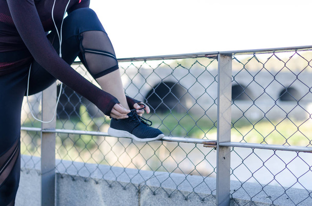 mujer atando cordones de zapatos mientras corre al aire libre y escuchando música con auriculares
 - Foto, Imagen