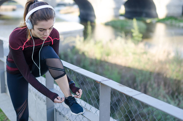 woman tying shoelaces while running outdoor and listening music with headphones - Zdjęcie, obraz