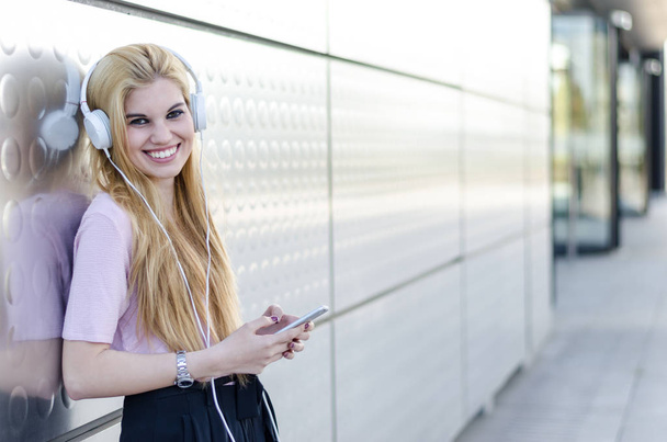 blonde woman listening music with headphones and mobile phone outdoor - Фото, зображення