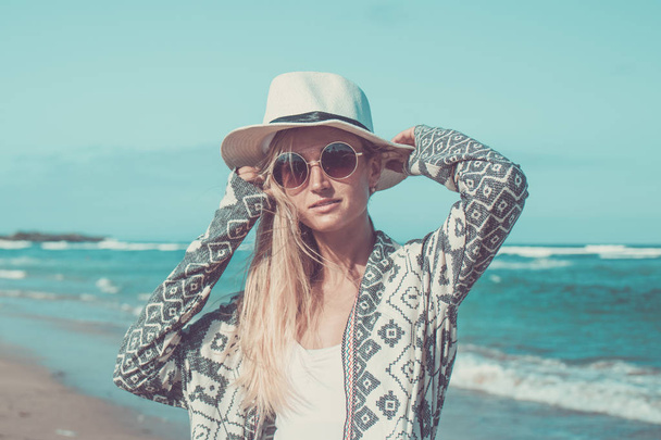 Porträt einer jungen sexy Frau mit weißem Hut und Sonnenbrille, die an einem sonnigen Tag am weißen Sandstrand einer tropischen Bali-Insel spaziert. Ozeankosten. - Foto, Bild