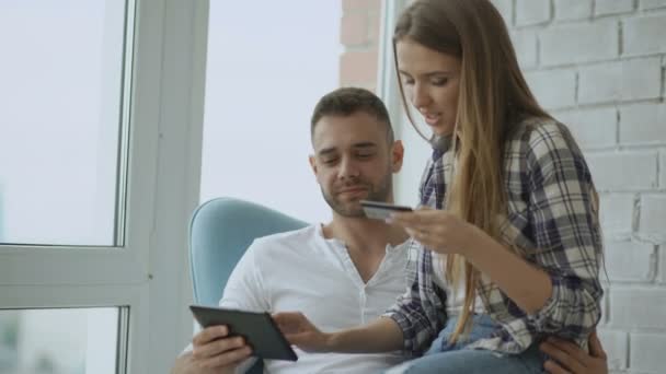 Young cheerful couple using digital tablet computer for online shopping sit on balcony in modern loft apartment - Záběry, video