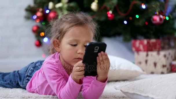 かわいい女の子のクリスマス ツリーの前でのスマート フォンを使用します。クローズ アップ ショット. - 映像、動画