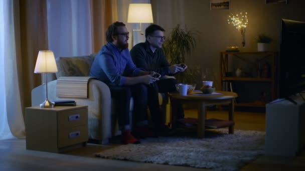 In the Evening Two Friends are Sitting on a Sofa in the Living Room and  Playing Competitive Video Games. One of Them Wins and He is Enjoying His Success. - Filmmaterial, Video