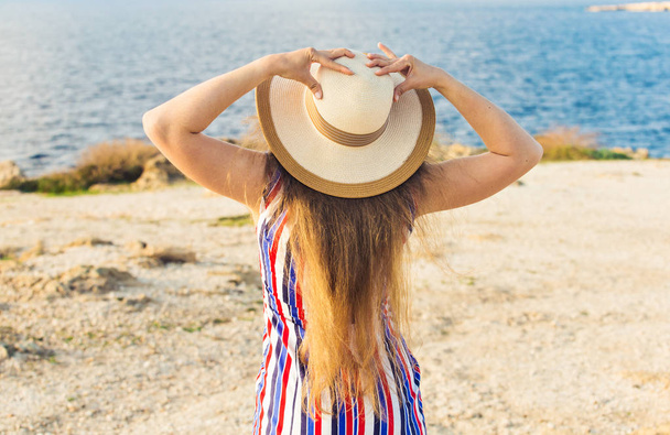 Young woman on the beach near the sea wearing dress and hat, rear view - Foto, imagen
