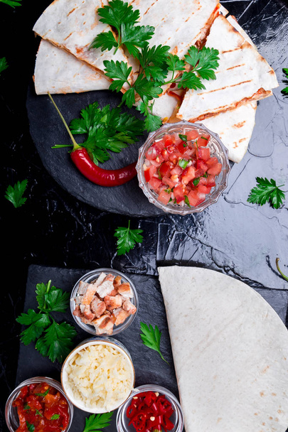 Mexican quesadilla and ingredients with salsa on black slate stone plate. Top view. - Photo, Image