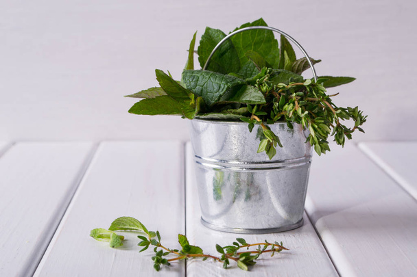 Свіжа м'ята, чебрець - ароматні кухонні трави в невеликому відрі на білому
 - Фото, зображення