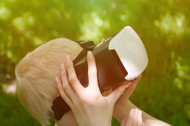 Moeder corrigeert zijn zoon bril van virtual reality tegen de achtergrond van groen - Foto, afbeelding