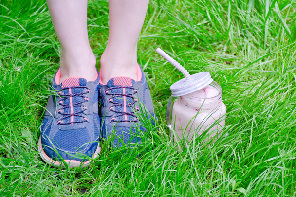 Pernas femininas em tênis e smoothies de morango na grama verde
 - Foto, Imagem