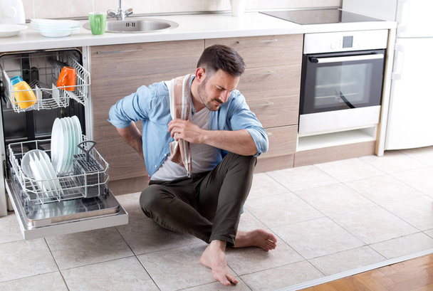 Уставший человек рядом с открытой посудомоечной машиной
 - Фото, изображение