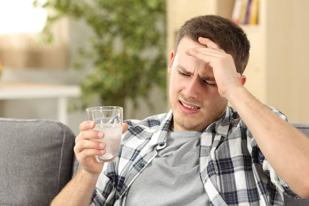 Mann mit Kopfschmerzen hält Schmerzmittel-Glas in der Hand - Foto, Bild