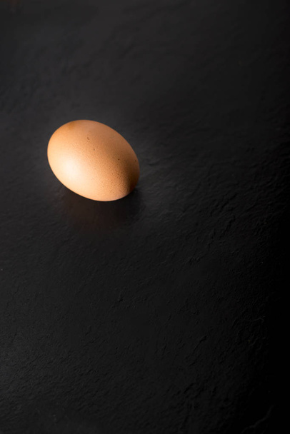 Kopya alanı ile siyah bir taş plaka üzerinde bir çiğ yumurta. - Fotoğraf, Görsel