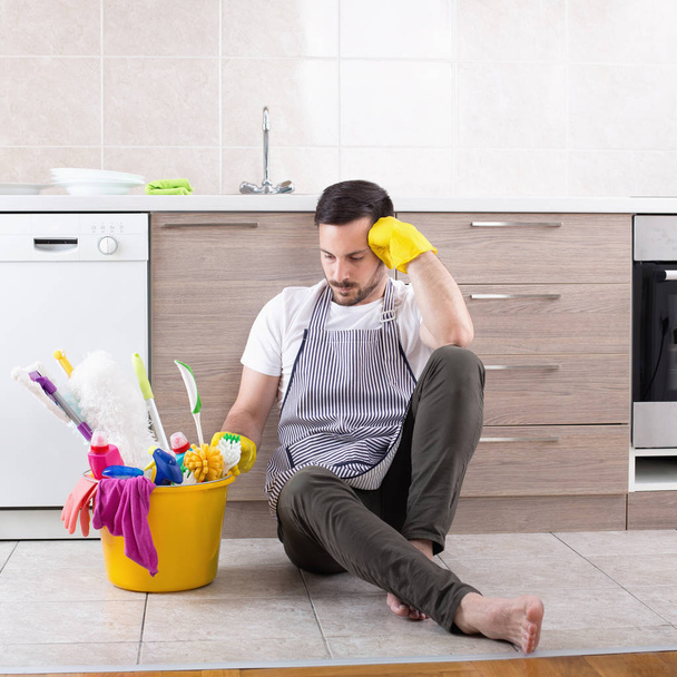 Tired man looking at cleaning equipment in kitchen - Photo, Image