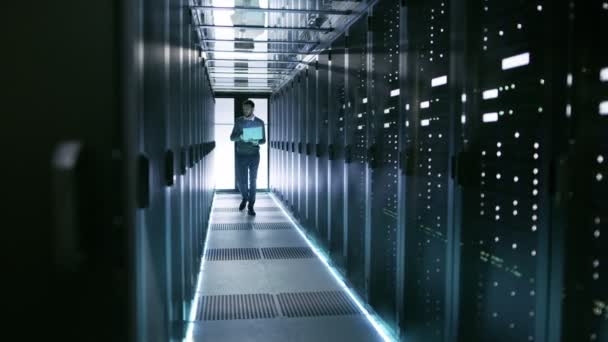 Ingeniero masculino del servidor camina con el ordenador portátil a través del centro de datos de trabajo lleno de servidores en rack
. - Metraje, vídeo