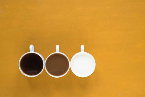 Three cups with coffee and milk on yellow background - 写真・画像